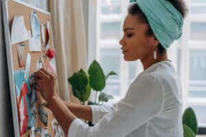 Woman pinning photos and inspiring images onto a vision board at home.