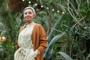 grey haired woman standing proud and calm in front of green plants